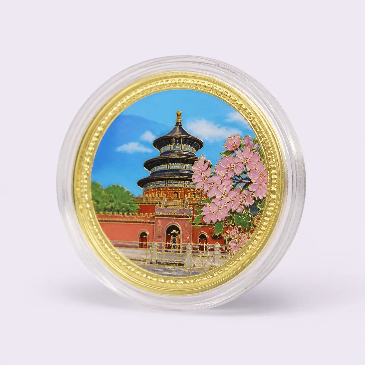 Gold souvenir medallion with raised temple and blossom artwork in a clear round capsule
